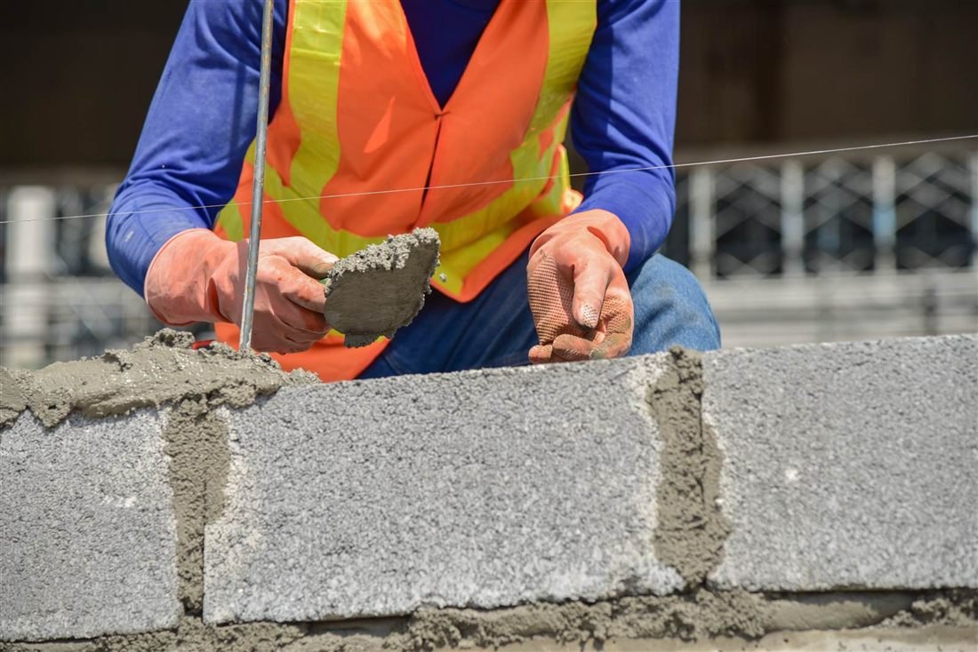 Operário assentando bloco de concreto com colher de pedreiro